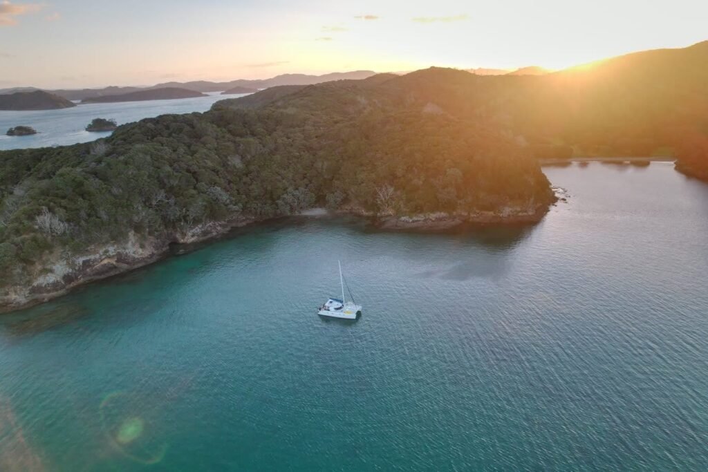 sun setting behind an island in the bay of islands with a catamaran anchored at a sheltered bay