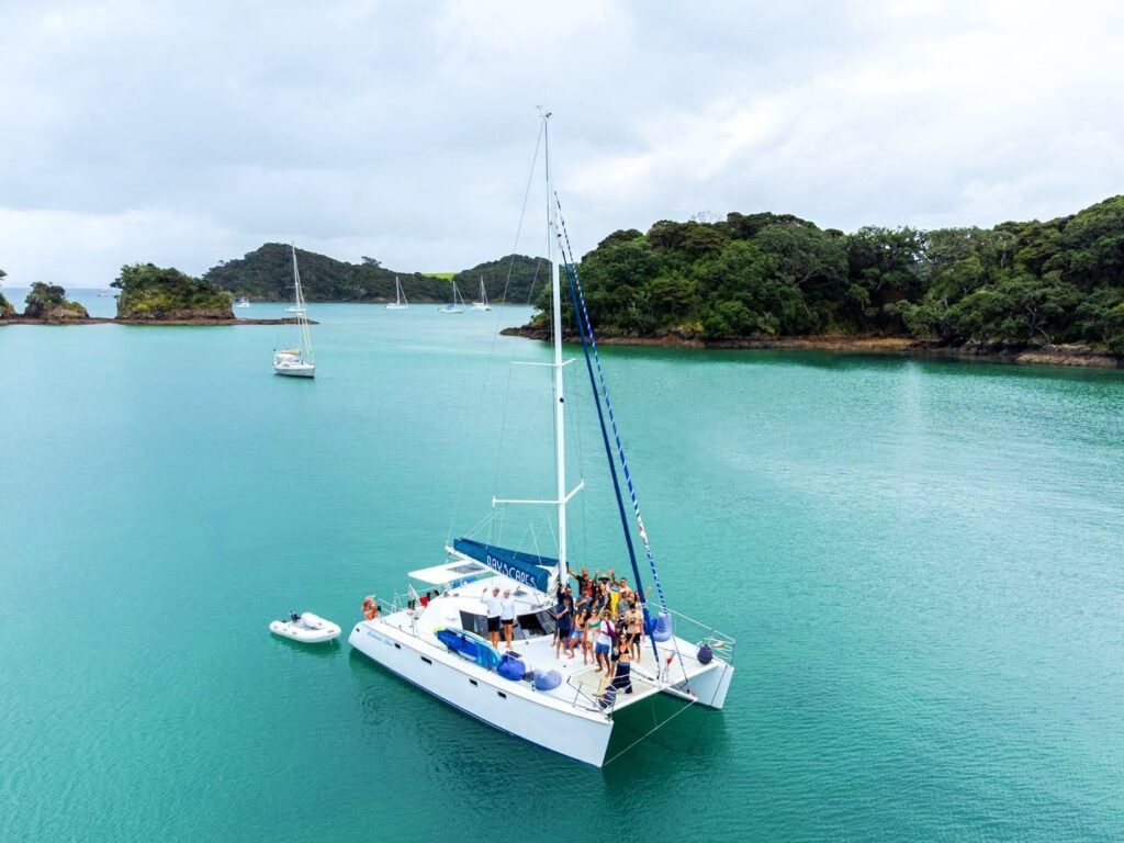 A catamaran at anchor in the Bay of Islands, featuring people on board waving