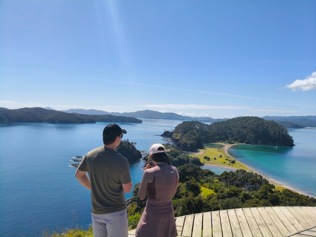 a couple stands at a lookout, viewing the twin lagoons on Roberton island in the Bay of Islands