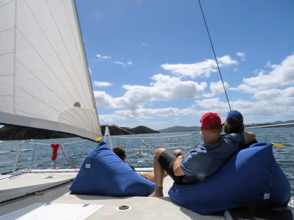 A couple sits on beanbags at the front of a catamaran, soaking up the sun and the serene ocean surroundings on a sailing charter in the Bay of Islands.